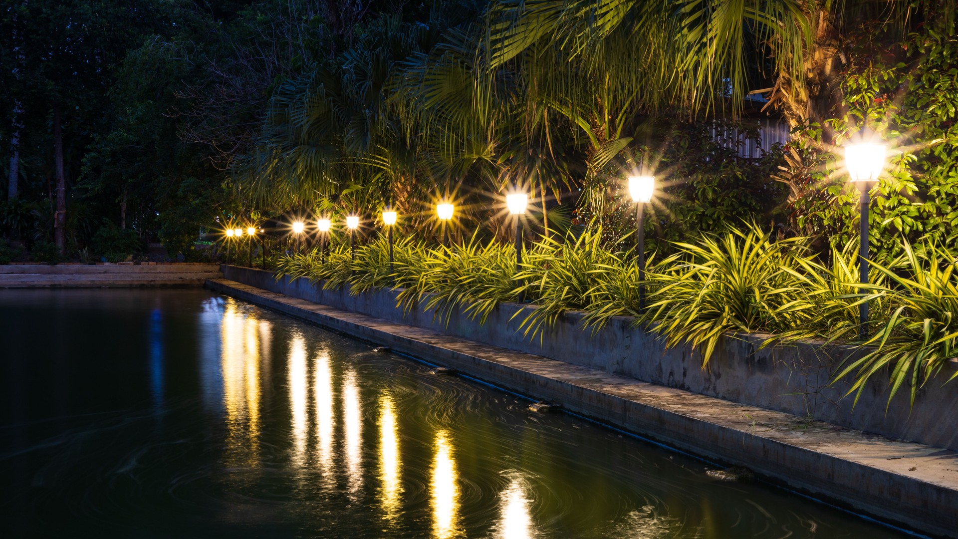 A view of the yellow light from the rows of lampposts decorated with gardens beside the pond.